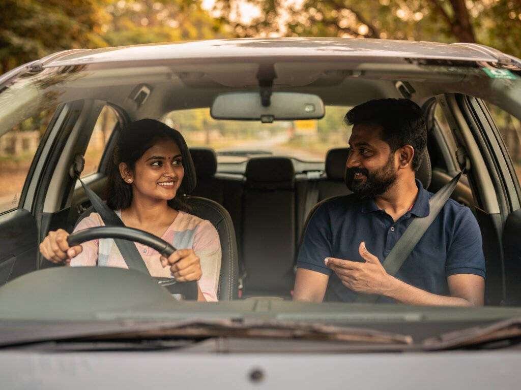 An instructor coaching a learner who is driving on a tree-lined road